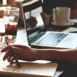 Copy Edits Someone holding a pen over their paper next to their computer during copy edits.